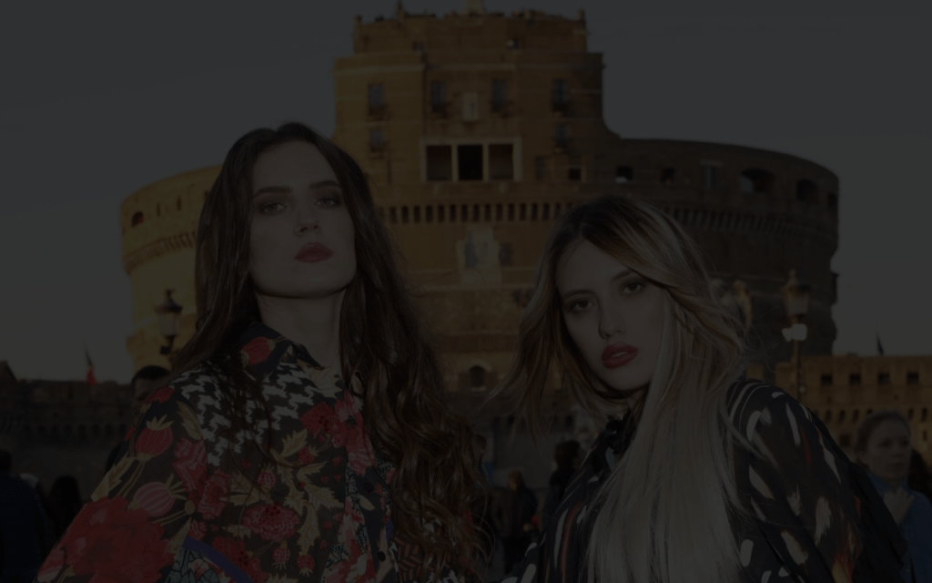 Due modelle con dei vestiti dai colori sgargianti sono in posa e mostrano delle acconciature con le extension e parrucche di Luxury Wigs.